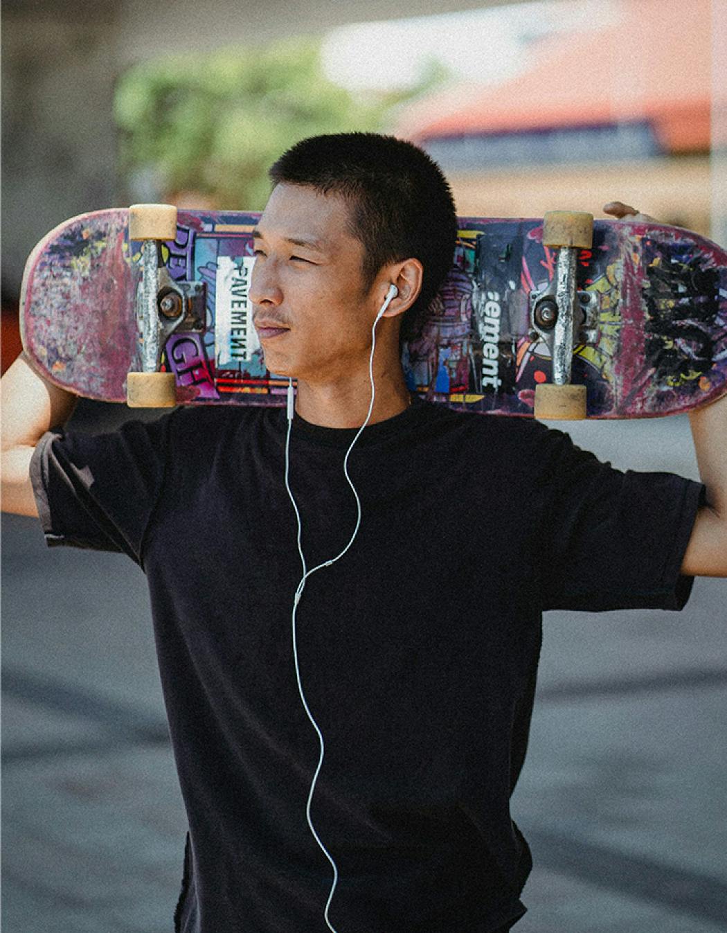 Junger Mann mit Kopfhörern, der ein Skateboard hält und entspannt.